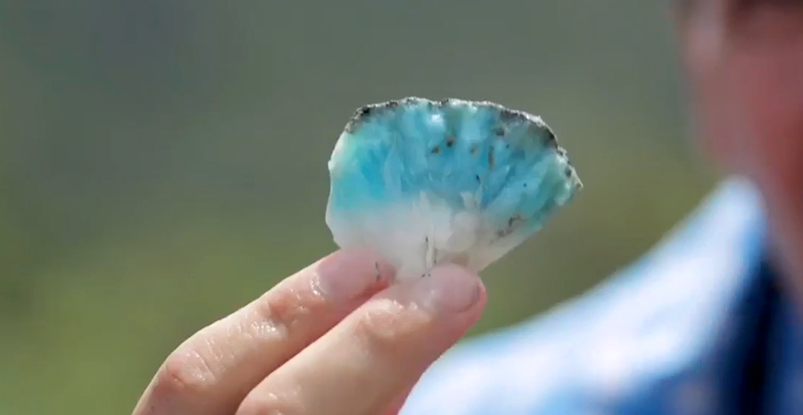 Someone is holding a slice of cut Larimar. It has white and blue marbling with rare specks of black.